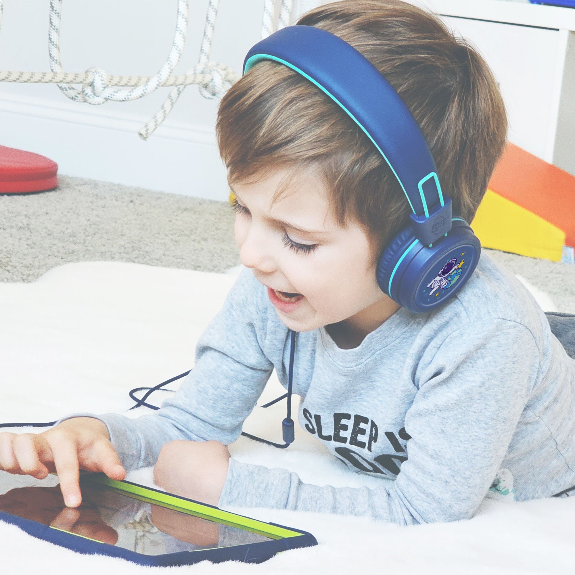 Child wearing Blue KJ55AUX headphones and using a tablet on a carpeted floor