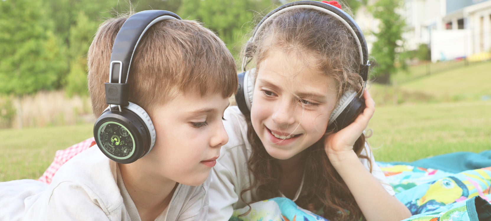 Kids wearing MEE audio KidJamz Share Bluetooth Wireless Headphones for Kids with Multipoint, LED Lights, 85dB Volume Limiter, Microphone, 40h battery; Childrens Headset for School/iPhone/iPad/Tablet  in a park setting