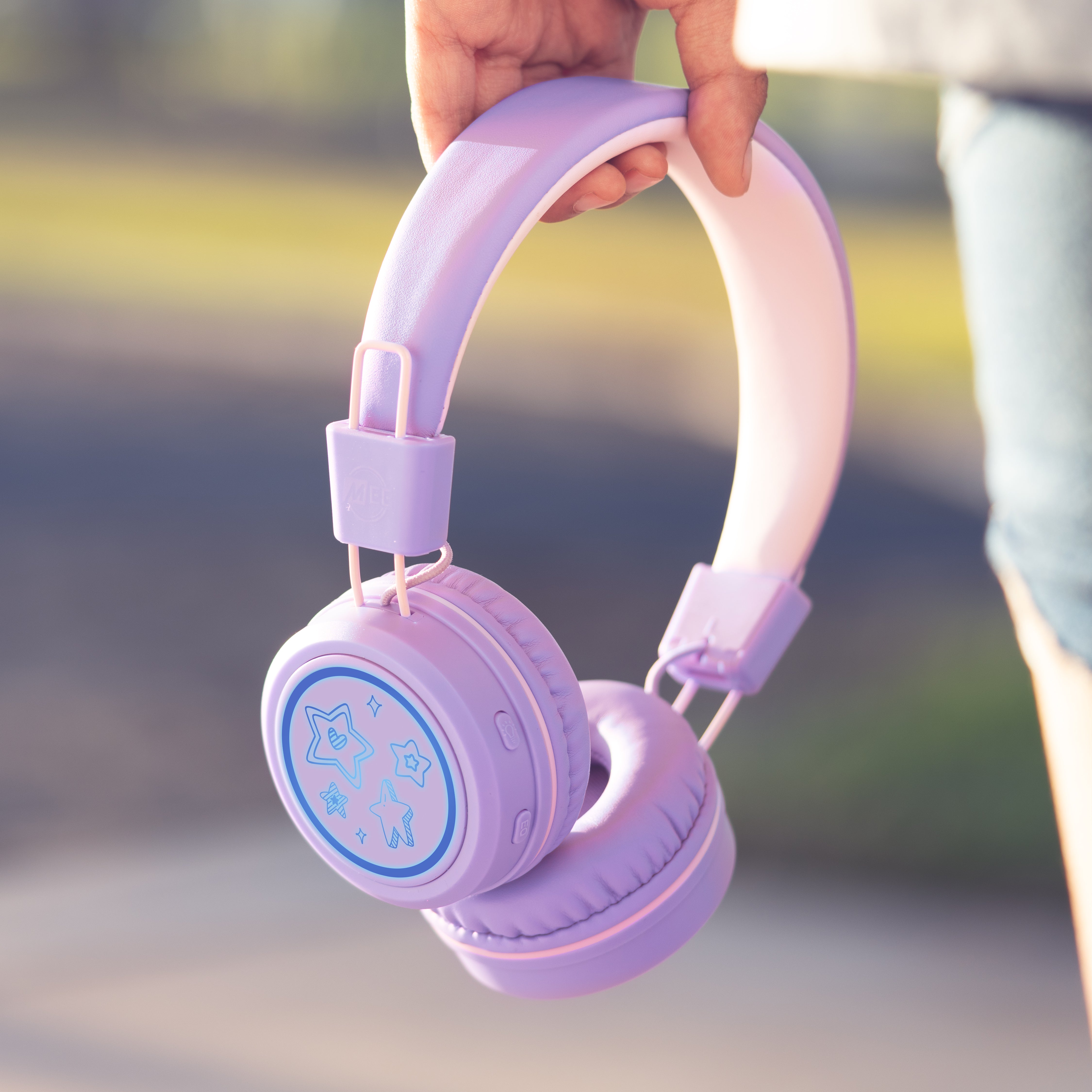 Image of a girl holding the MEE audio KidJamz KJ55BT Bluetooth Wireless Safe Listening Headphones for Children with LED Lights, 85dB Volume Limiter, Microphone, & 40h battery; Kids Headset for School / iPhone / iPad / Tablet