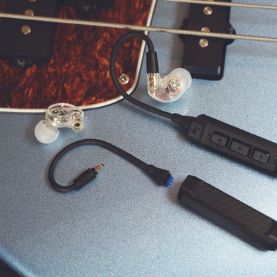 MEE audio M6 PRO Musicians' In-Ear Monitors Wired + Wireless Combo Pack: Includes IEMs, 2 Audio Cables and BT3 Hi-Res Bluetooth Audio Adapter w/aptX, LDAC, Auracast Support, & Built-In Headset (Clear) displayed on a guitar 