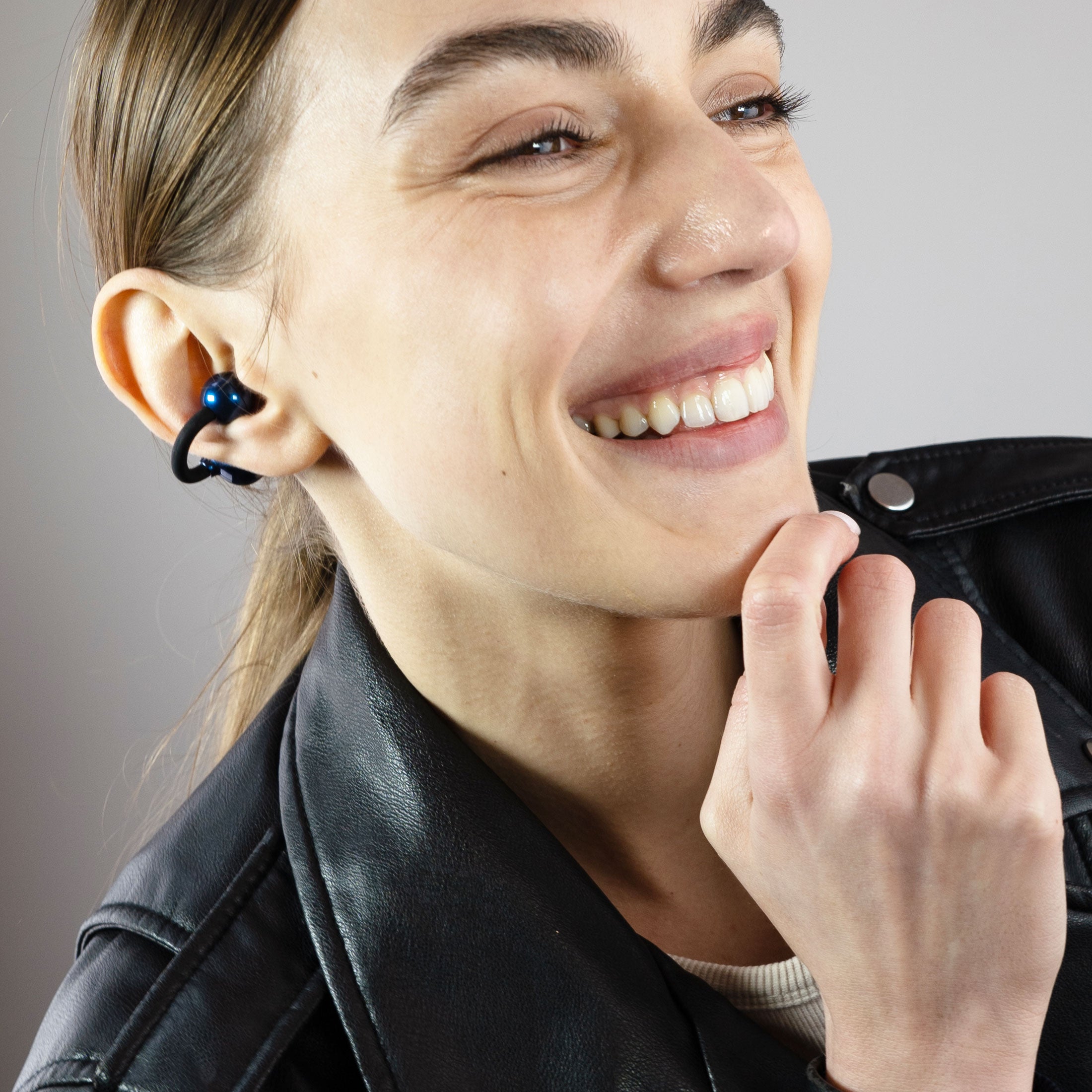 Close-up of a woman wearing a black Pebbles Air earbud while smiling
