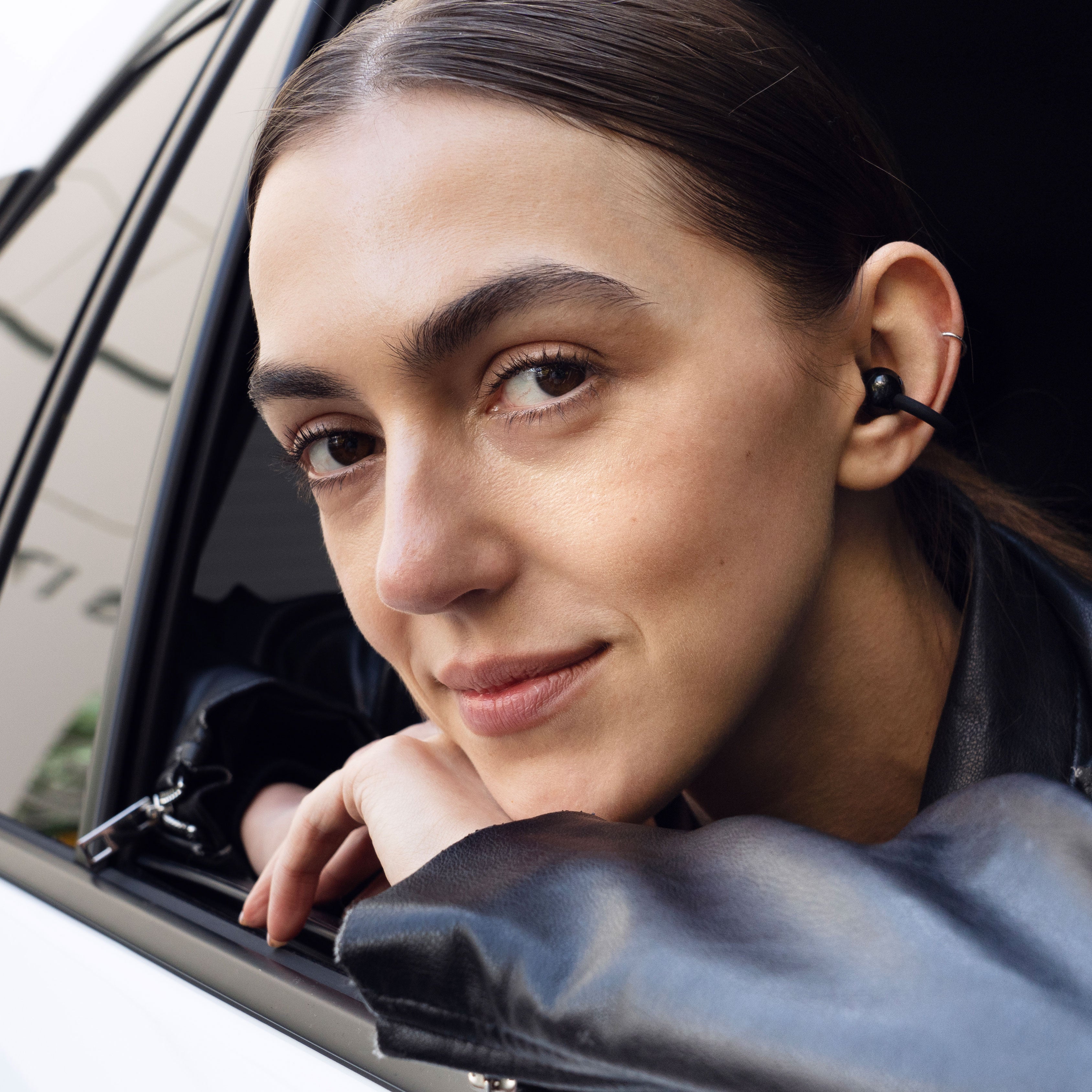 Woman with a Pebbles Air earbud peeking out of a car window

