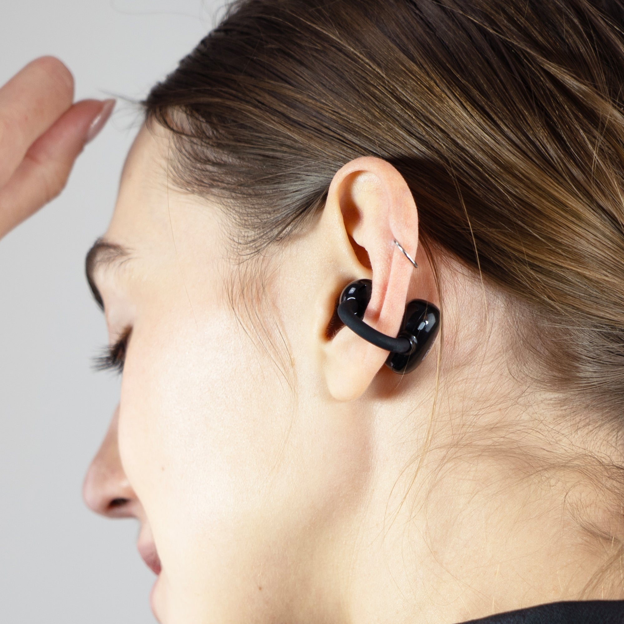 Person wearing a black Pebbles Air earbud with a neutral background