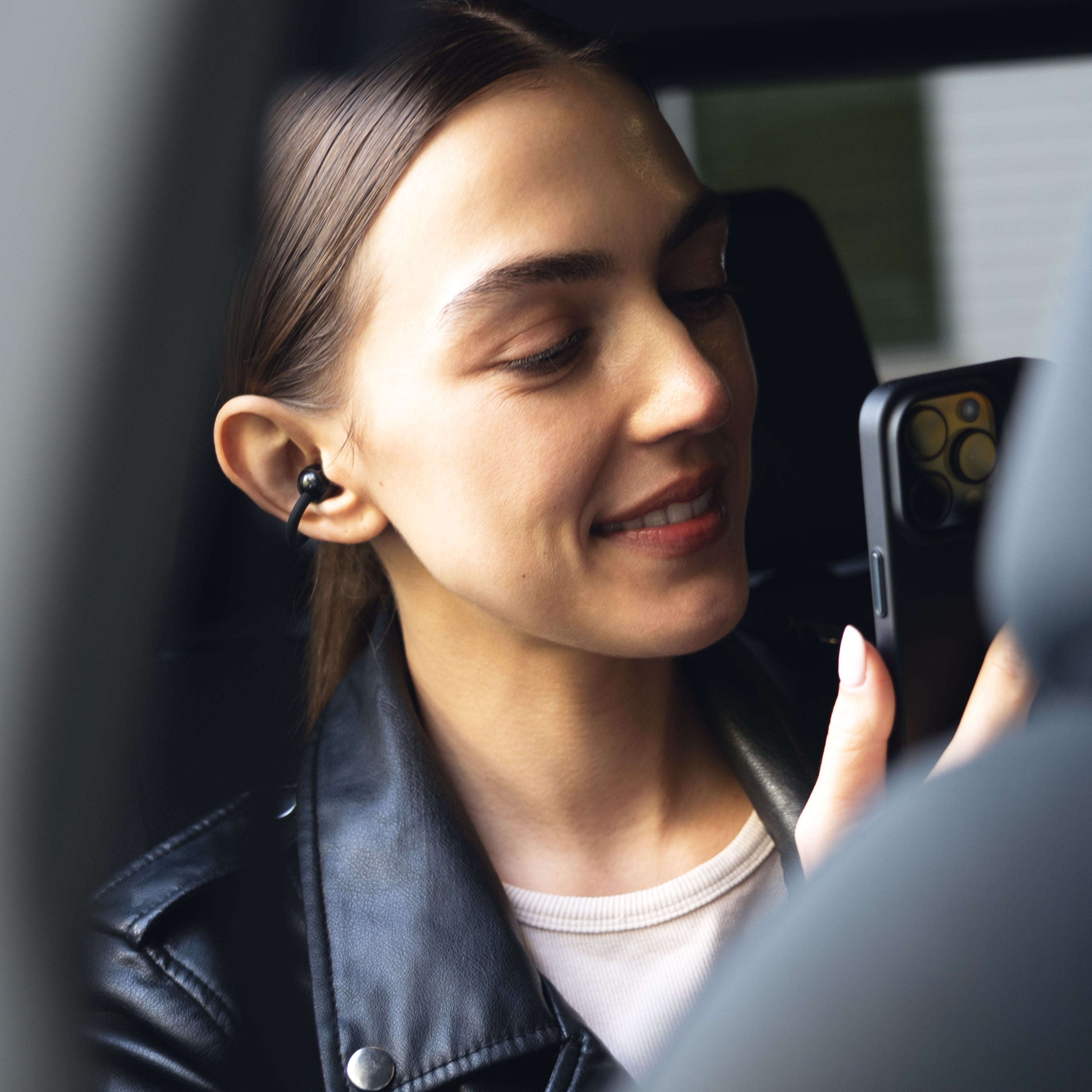 Woman sitting in a car, looking at her phone with a smile while wearing black Pebbles Air 