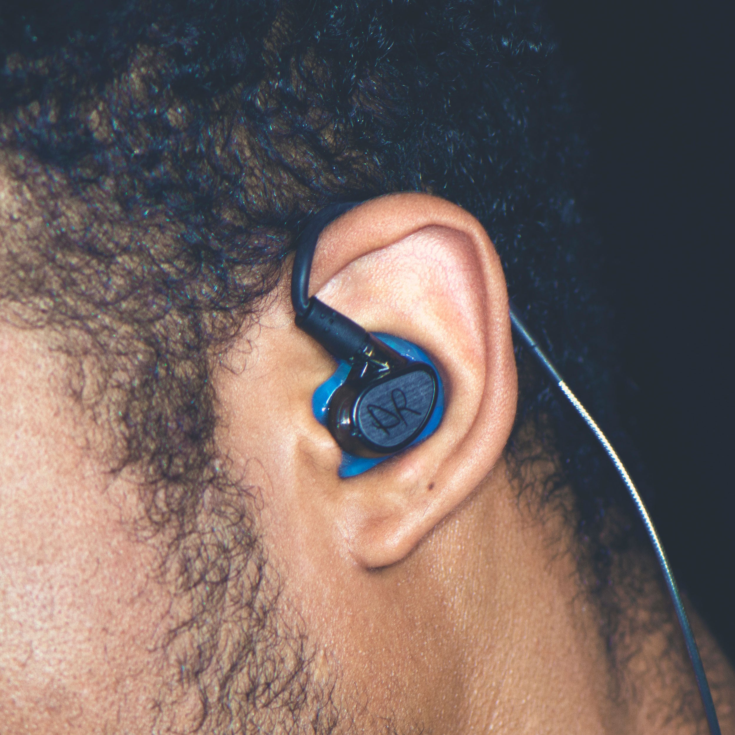 Close-up of a man wearing blue custom eartip on an MX PRO in-ear monitor with a custom faceplate on a dark background