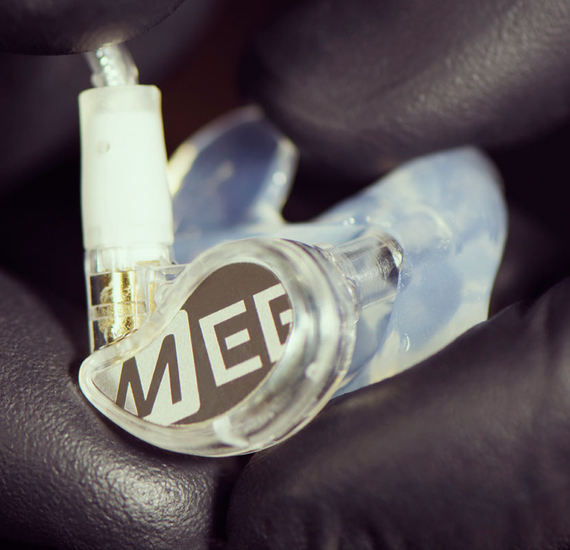 Close-up of a custom in-ear monitor with a transparent casing and a white cable, featuring the logo "mee" on its side, resting on a textured surface.