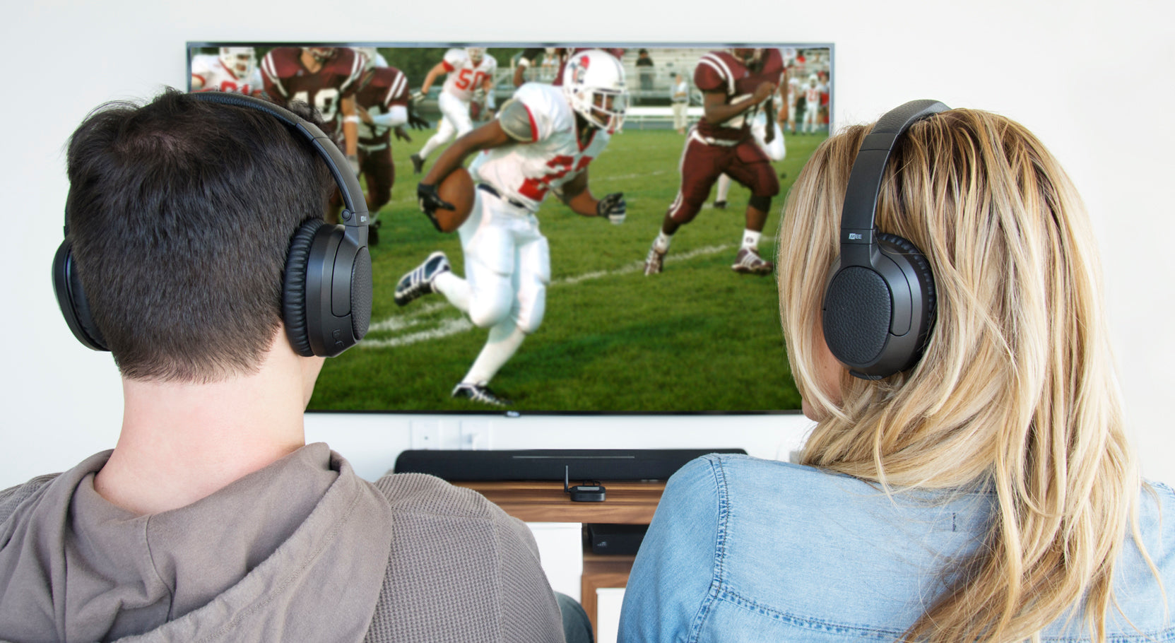 A man and a woman wearing headphones are watching a football game on a tv. the screen shows players in a football match.