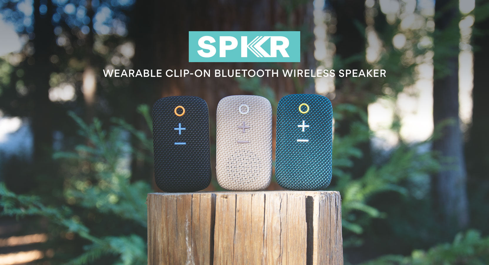 Promotional image of three spkr wearable clip-on bluetooth wireless speakers, displayed on a wooden stump with a blurred forest background. the speakers are in black, white, and blue colors.