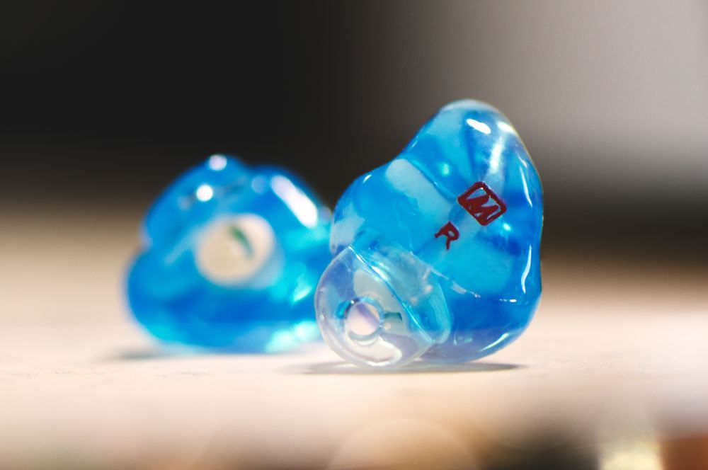 Close-up of custom blue earplugs on a table, marked with "r" to denote the right earpiece.