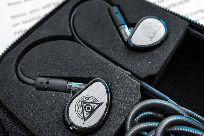 A pair of high-end in-ear headphones with a distinctive triangular logo, neatly placed in a custom foam case, prominently displaying the metallic and black design.