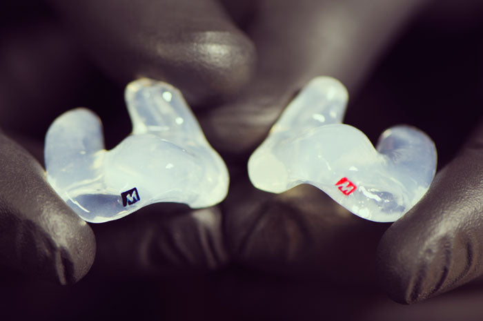 A close-up of two custom-made dental mouthguards held by gloved hands, one marked with an 'm' and the other with an 'r'.
