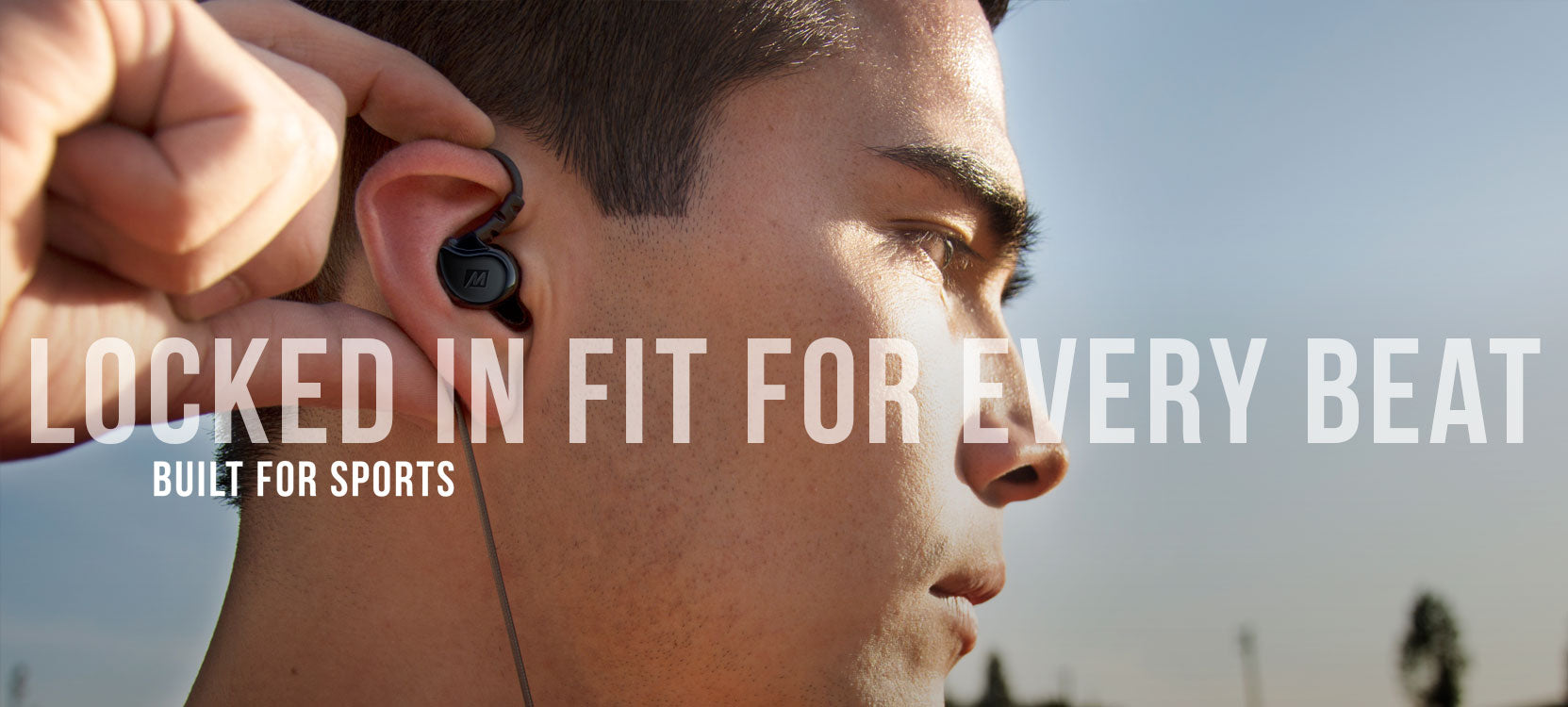 Close-up of a young man's profile as he adjusts a wireless earbud in his ear, with text overlays saying "locked in fit for every beat" and "built for sports".