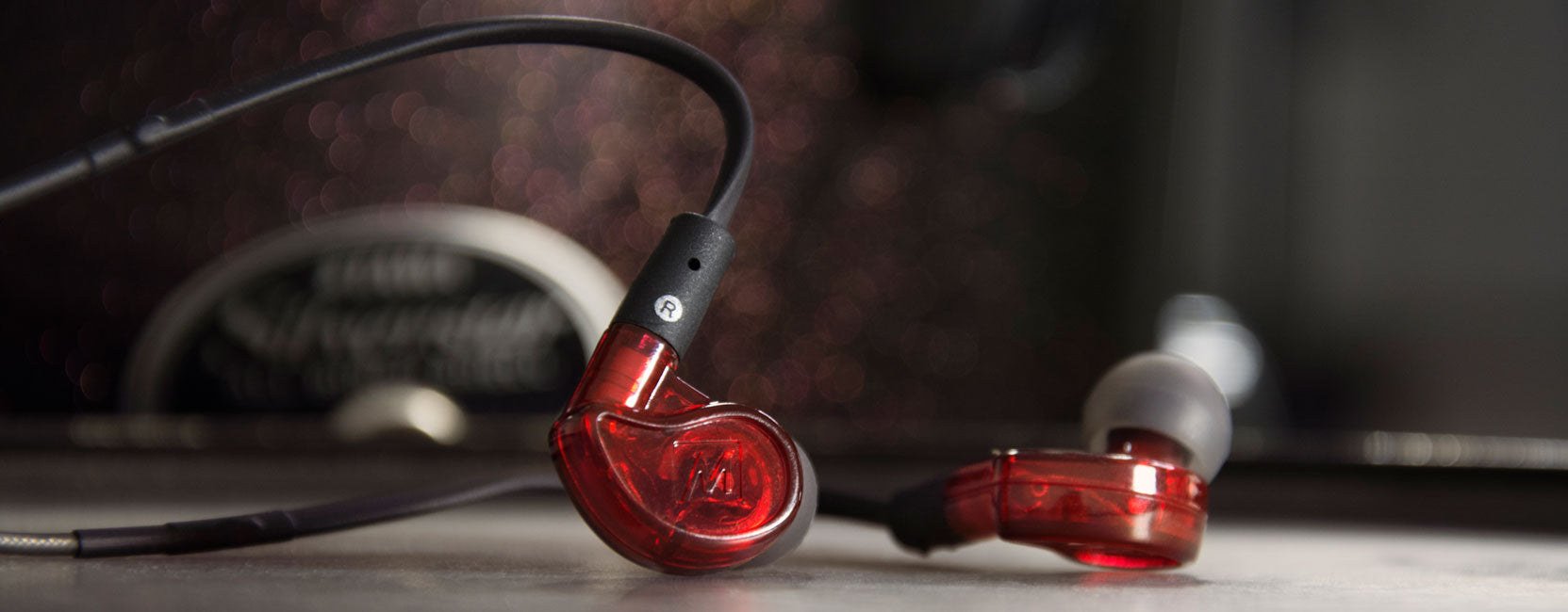 Close-up of red in-ear headphones with a clear casing, resting on a reflective surface against a blurred background with dark tones.